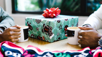 two people drinking coffee during the holidays exchanging a wrapped gift